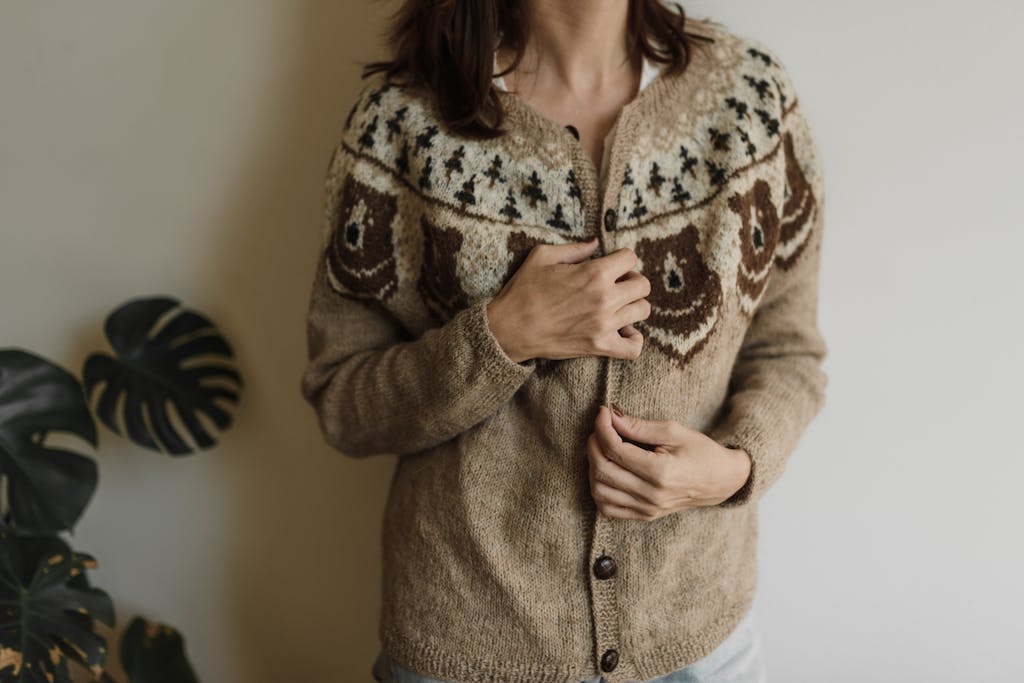 A woman gently holds her knitted cardigan, showcasing detailed handmade patterns in warm colors.
